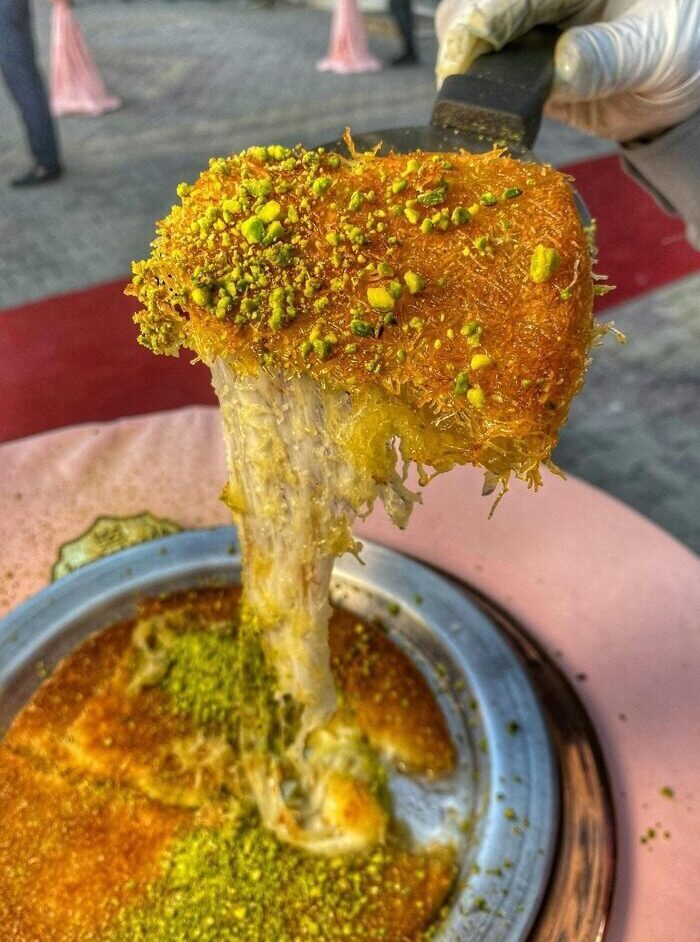 Close-up of melting kunefe, a traditional Middle Eastern dessert with crispy layers of pastry, melted cheese, and sweet syrup.