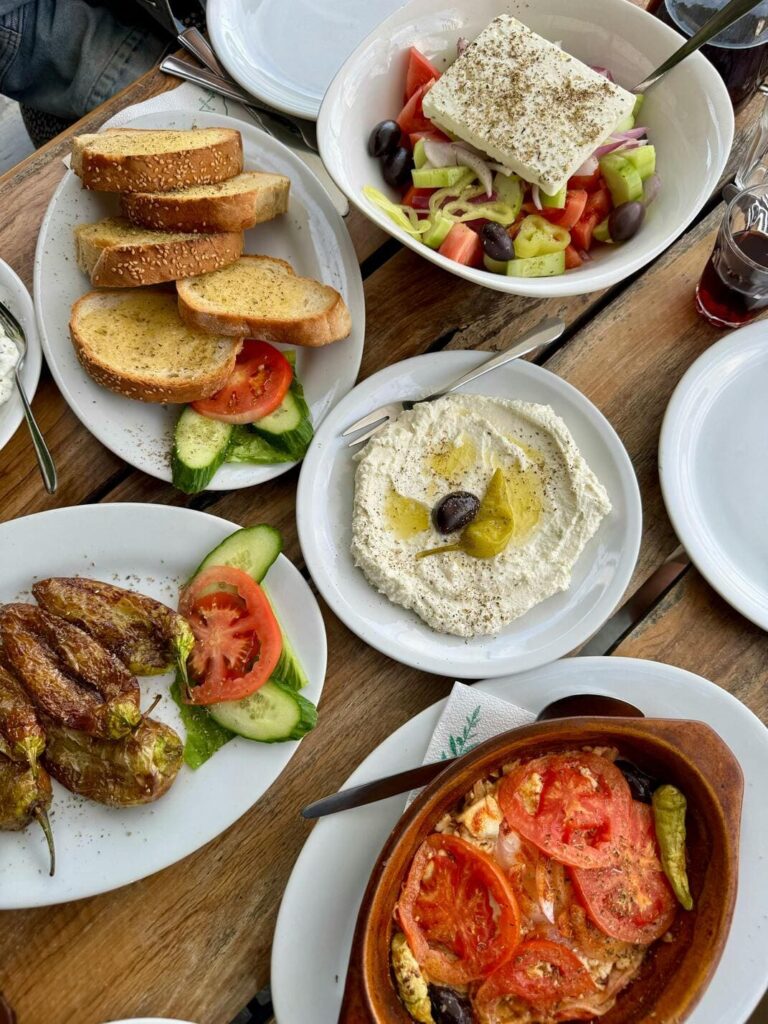 A table filled with traditional Greek dishes, including fresh salads, hummus dip, and mezze.