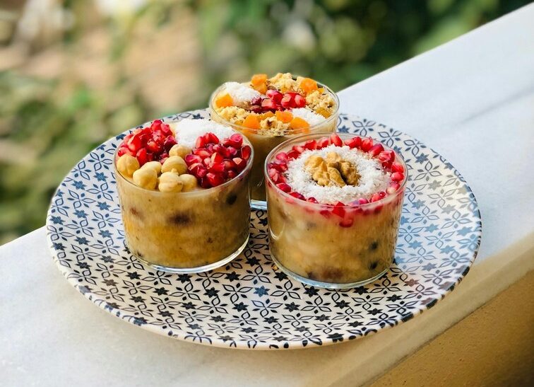 Three cups of ashure, a traditional Turkish dessert made with grains, nuts, and dried fruits, served in clear cups showcasing the colorful, layered ingredients.