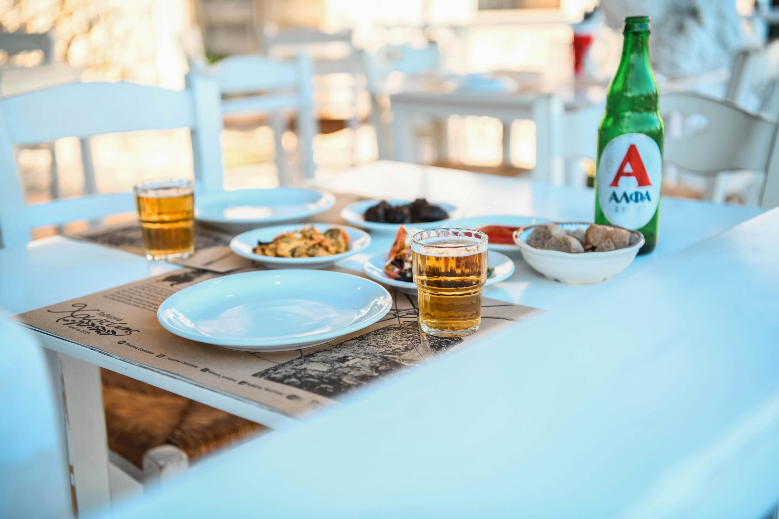 Greek taverna table with dishes and beer – A lively Greek taverna table set with local dishes and glasses of beer, capturing the essence of Thessaloniki’s food scene.
