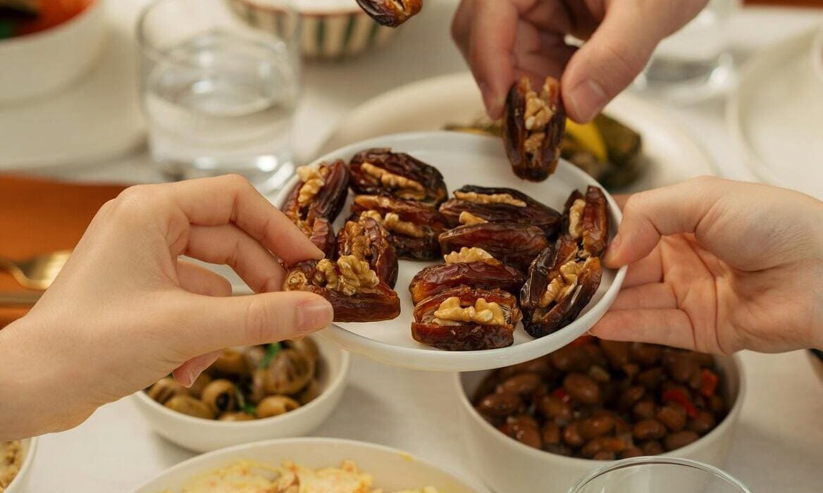 People holding dried dates filled with walnuts above a serving plate, showcasing the traditional Middle Eastern treat made with sweet, soft dates and crunchy walnut filling.