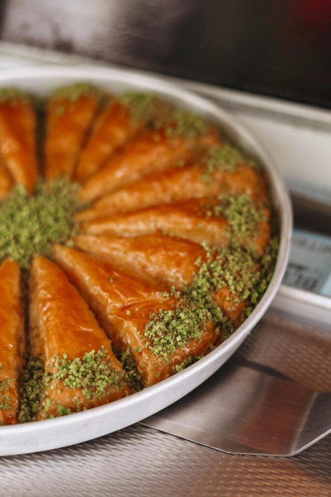 Close-up of a plate of pistachio-sprinkled baklava, highlighting its golden, crispy layers and vibrant green pistachios atop the rich, syrup-soaked pastry.
