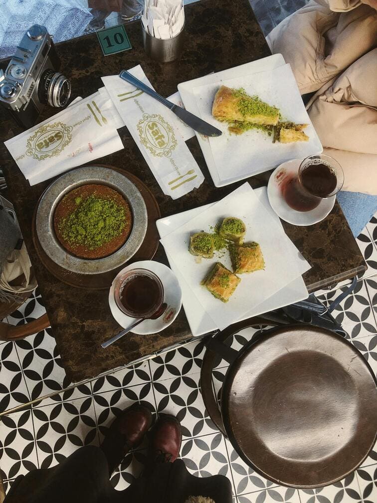 Traditional Turkish pastry shop table, featuring plates of kunefe, a sweet cheese dessert, and glasses of Turkish tea, capturing the essence of Turkish dessert culture.