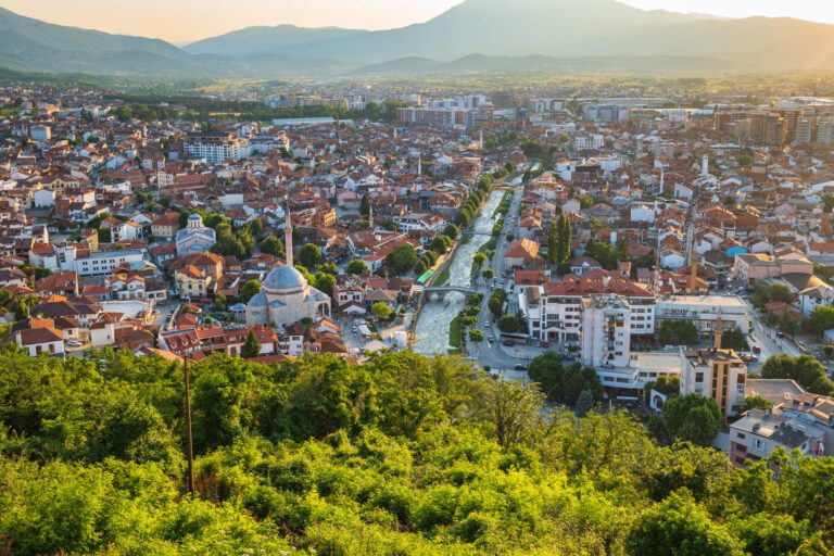 Panoramic landscape view of Prizren, Kosovo, in spring, highlighting the historic town, rolling green hills, and a picturesque river.