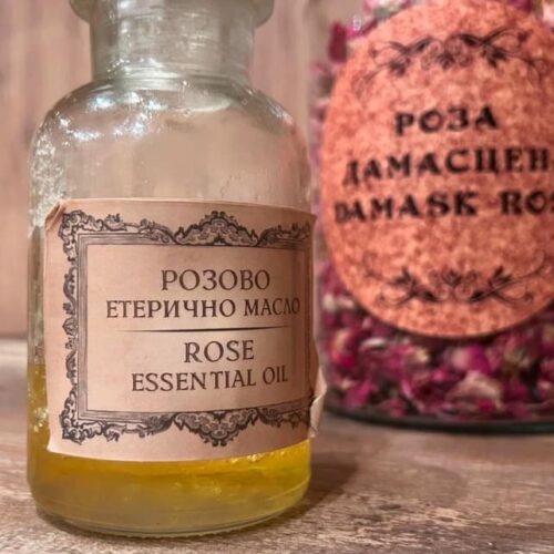 A small glass jar filled with golden rose oil sits on a rustic wooden surface.