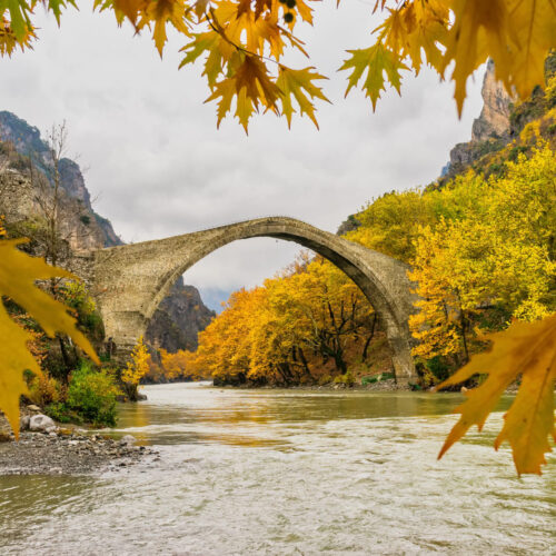 An old-time stone bridge in Zagorochoria, northern Greece, above a fully flowing river, surrounded by beautiful coloured autumn trees