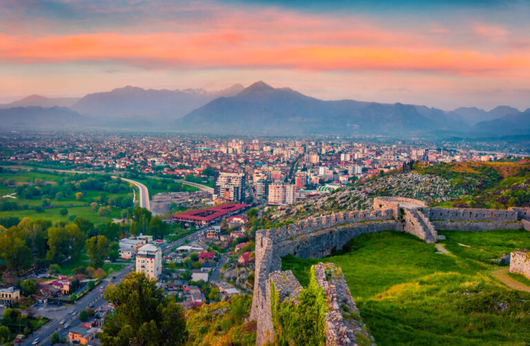 Cityscape of Tirana at sunset, with distant mountains and the capital’s skyline in view.